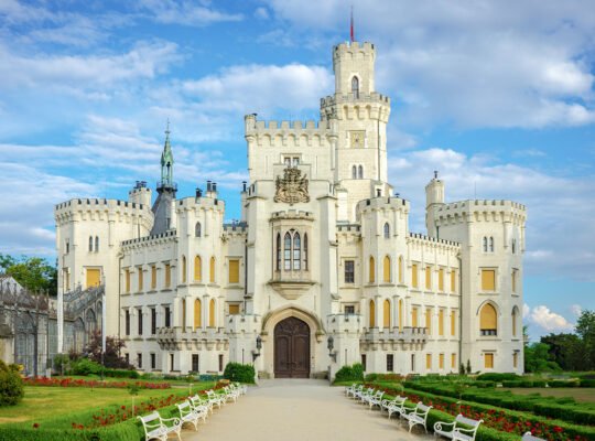 Front facade of Hluboka Castle with gardens under a blue sky