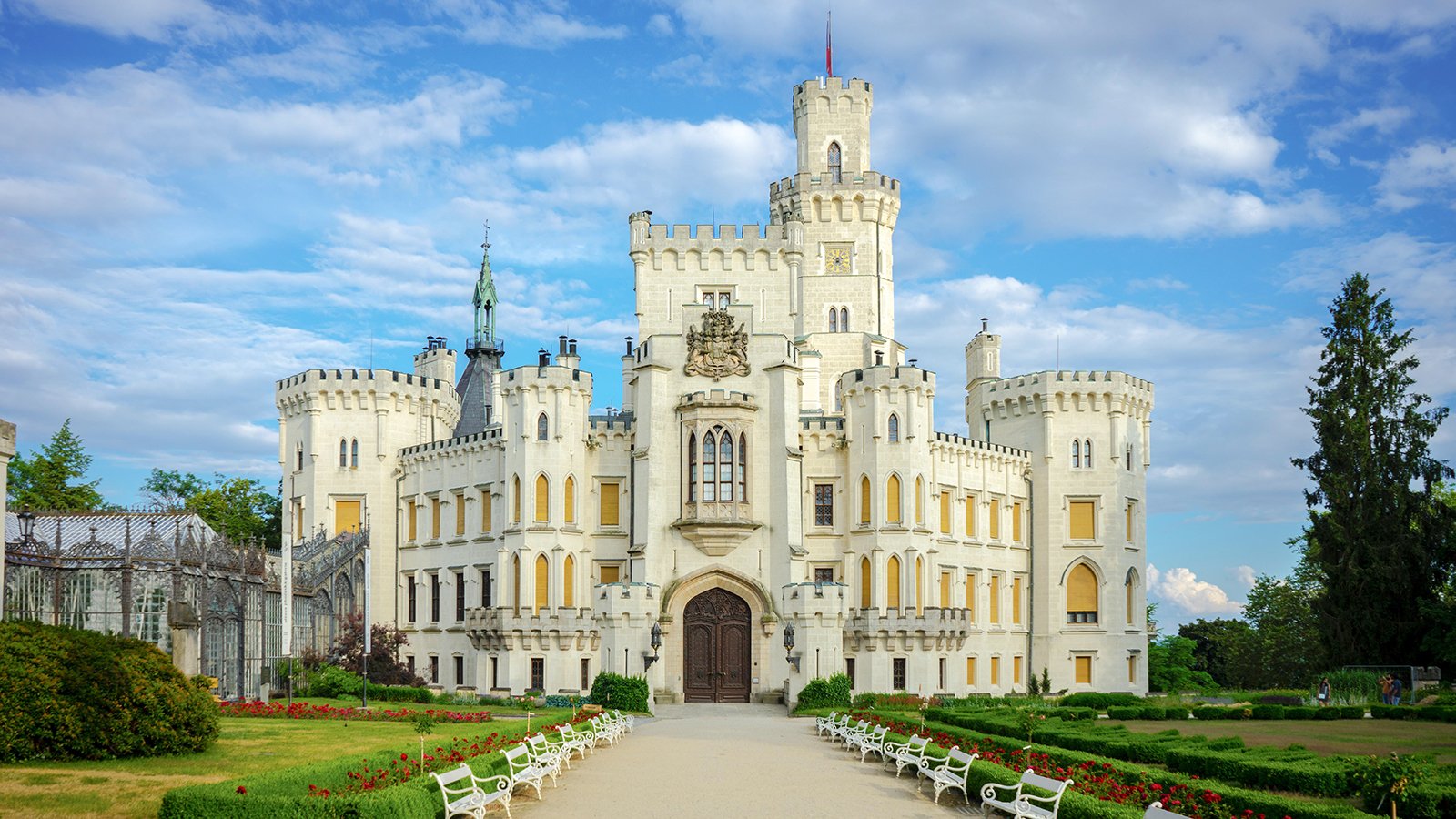 Front facade of Hluboka Castle with gardens under a blue sky