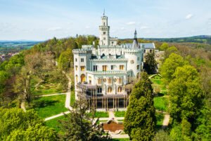 Aerial view of Hluboka Castle surrounded by green trees and gardens