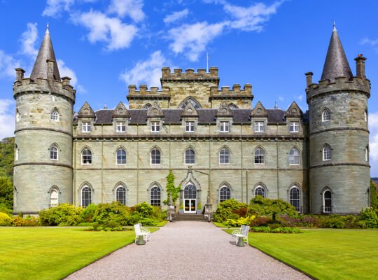 Front facade of Inveraray Castle with towers and manicured lawns under blue sky