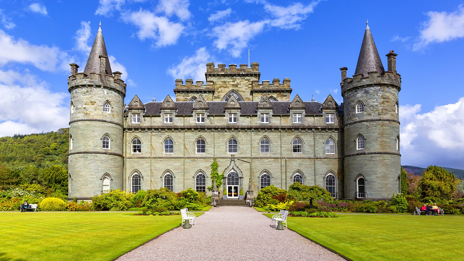 Front facade of Inveraray Castle with towers and manicured lawns under blue sky