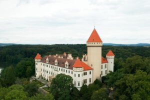 Aerial view of Konopiste Castle with red roofs amid dense green forest