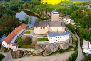 Aerial view of Kost Castle perched on rocky cliff above a secluded pond