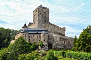 Stone towers of Kost Castle rising above green trees under cloudy sky