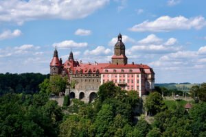 Ksiaz Castle perched above wooded valley under a blue sky
