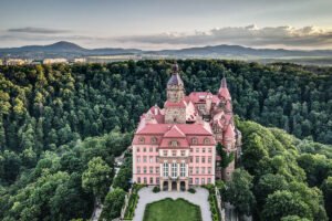 Aerial view of Ksiaz Castle surrounded by dense forest and distant mountains