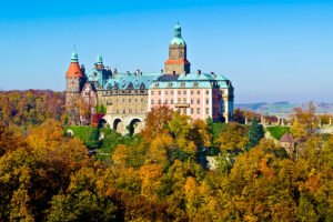 Ksiaz Castle perched above autumn forest, stone arches and copper roofs under clear blue sky