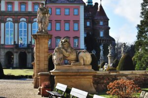 Stone lion statue by pink Ksiaz Castle facade in sunny formal gardens
