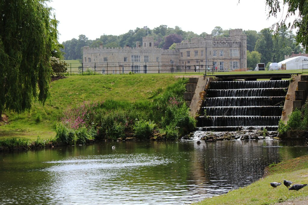 Leeds Castle across a tranquil moat with stepped waterfall and pigeons
