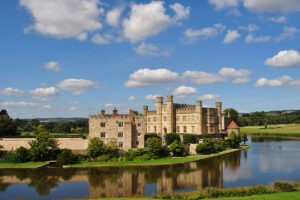 Leeds Castle beside reflective moat under blue sky