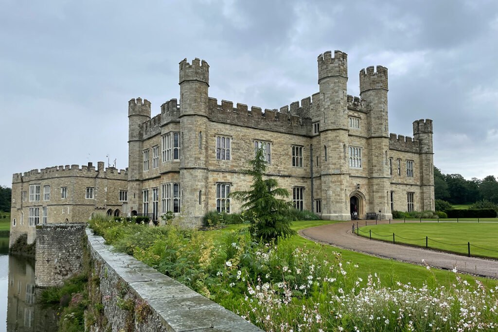 Leeds Castle beside moat and gardens under cloudy sky