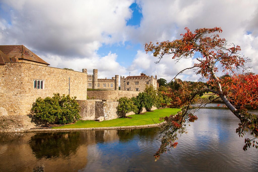 Leeds Castle beside reflective moat with autumn tree