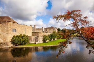Leeds Castle beside reflective moat with autumn tree
