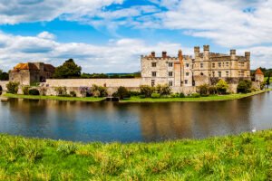 Leeds Castle on island surrounded by reflective moat under blue sky