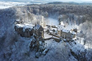 Aerial view of Lichtenstein Castle perched on snowy cliff amid frosted forest