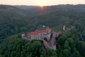 Aerial view of Pernstejn Castle at sunset atop forested ridge