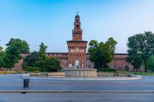 Front facade of Sforzesco Castle with fountain and trees at dawn