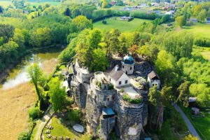 Aerial view of Sloup Castle atop rocky sandstone cliff surrounded by trees