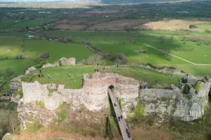 Aerial view of Beeston Castle ruins atop rocky hill with visitors on bridge