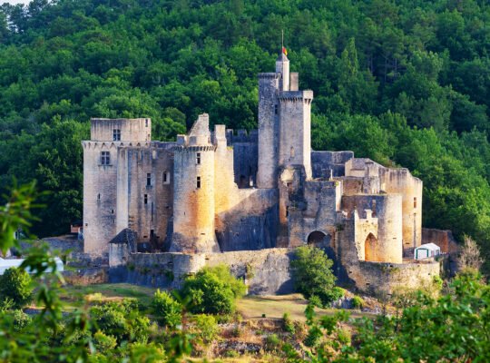 Bonaguil Castle perched on wooded hilltop at sunset