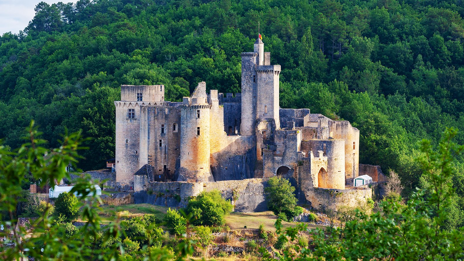 Bonaguil Castle perched on wooded hilltop at sunset