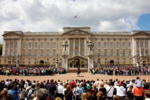 Buckingham Palace gates with crowd and guards under cloudy sky