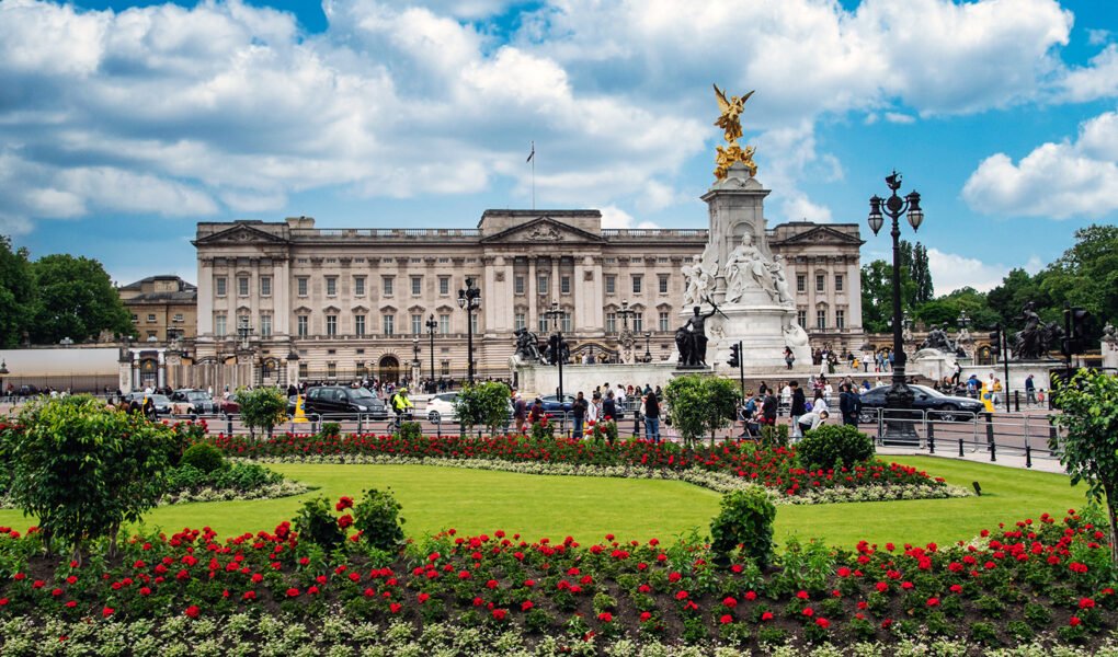 Buckingham Palace façade with Victoria Memorial and flowerbeds under blue sky