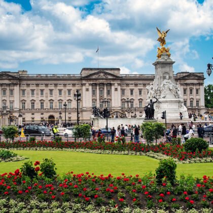 Buckingham Palace façade with Victoria Memorial and flowerbeds under blue sky