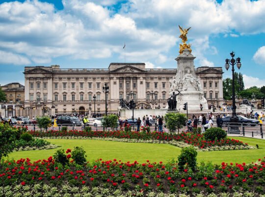 Buckingham Palace façade with Victoria Memorial and flowerbeds under blue sky
