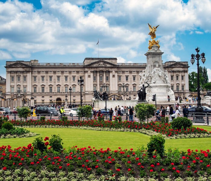 Buckingham Palace façade with Victoria Memorial and flowerbeds under blue sky