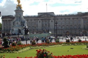 Buckingham Palace facade behind Victoria Memorial and red flowerbeds, visitors strolling