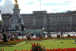 Buckingham Palace facade behind Victoria Memorial and red flowerbeds, visitors strolling
