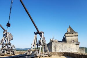 Medieval trebuchets and Château de Castelnaud under blue sky