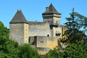Stone towers of Château de Castelnaud framed by trees under blue sky