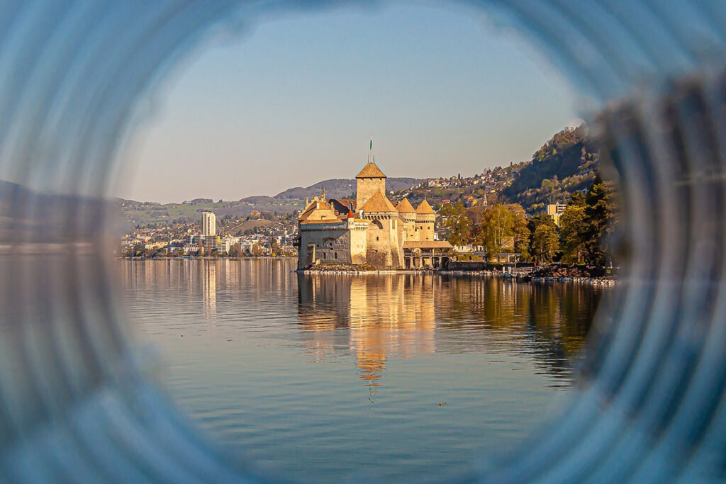 View of Chillon Castle reflected on calm Lake Geneva through circular frame