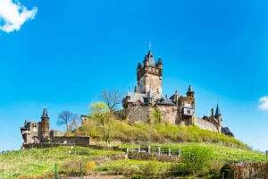 Cochem Castle perched on green Moselle hillside under clear blue sky