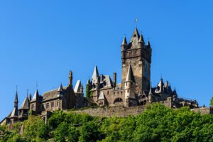 Cochem Castle on hill above green trees against blue sky
