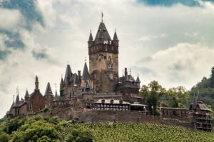 Cochem Castle on a hill above Moselle vineyards under cloudy sky