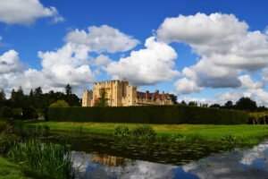 Hever Castle beside reflective moat under blue sky