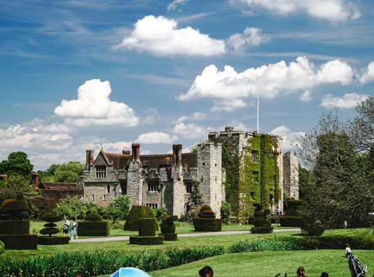 Hever Castle beside manicured gardens under a bright blue sky
