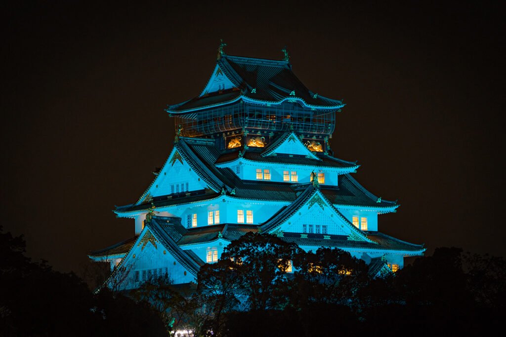 Illuminated Osaka Castle glowing blue against night sky