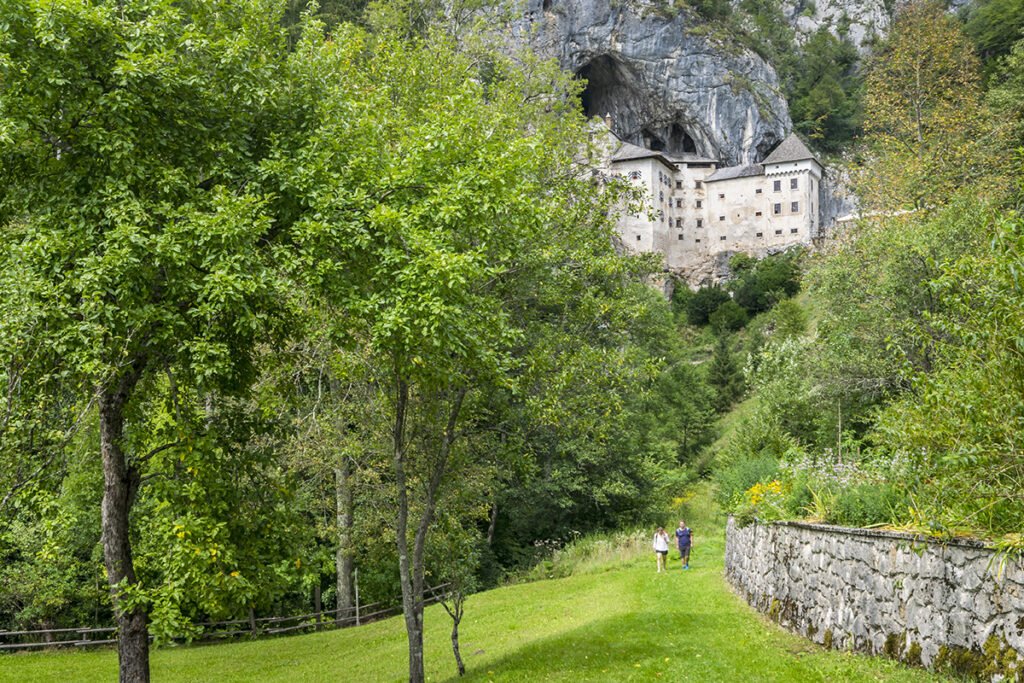 Predjama Castle built into limestone cliff, hikers below