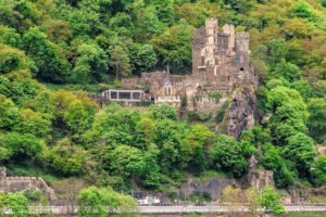 Rheinstein Castle perched on forested Rhine hillside overlooking road and river