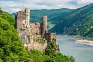 Rheinstein Castle perched on rocky Rhine cliff above river and green hills