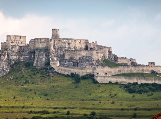 View of Spiš Castle ruins atop rocky hill under cloudy sky