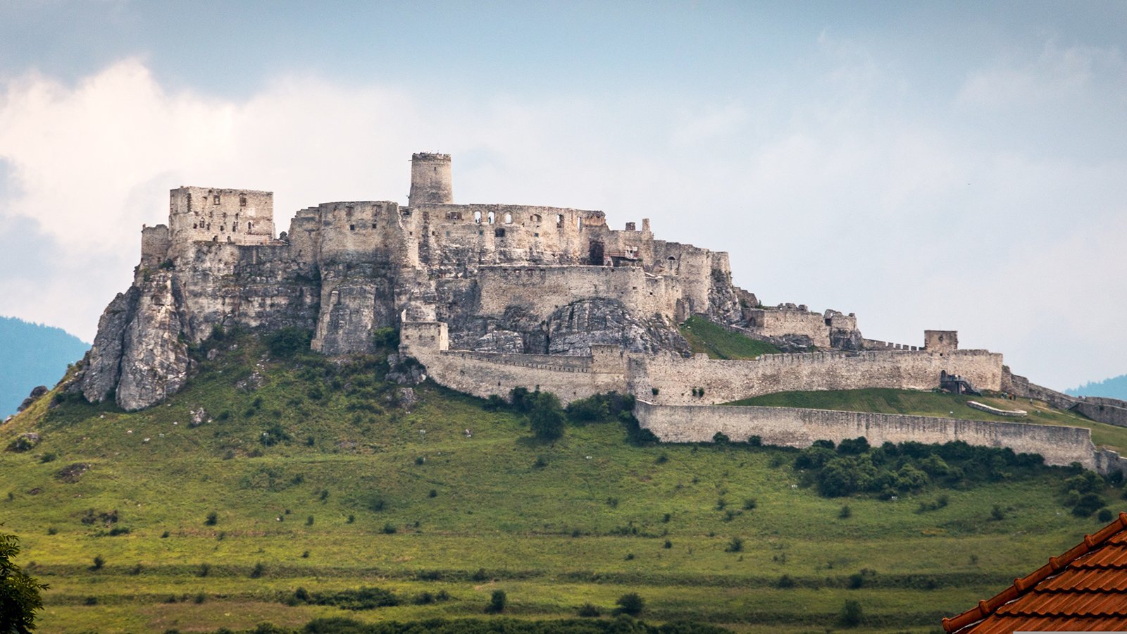 View of Spiš Castle ruins atop rocky hill under cloudy sky