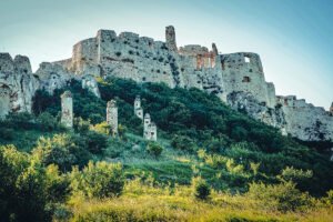 View of Spiš Castle ruins rising above green hillside at sunrise