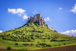 Spiš Castle ruins atop green hill under blue sky