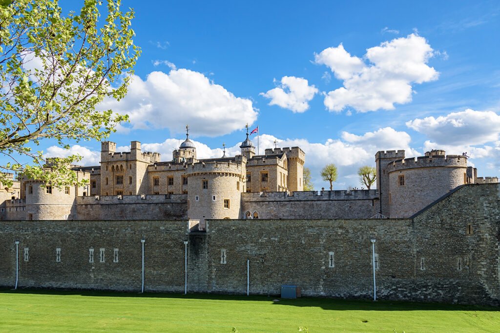 The Tower of London seen from grassy moat under blue sky