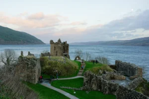 Ruined Urquhart Castle overlooking Loch Ness, grassy paths and visitors at dusk